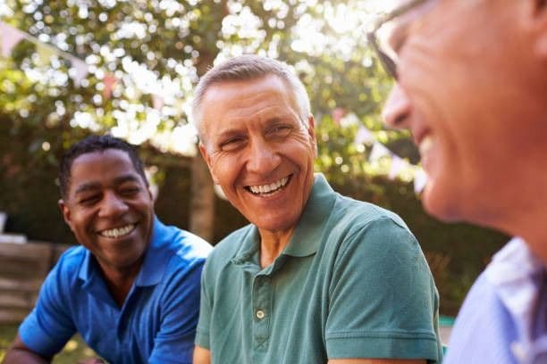 Three men sitting outdoors, smiling and enjoying a conversation in a pleasant setting.