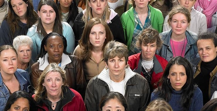 A large group of women of diverse appearances, all looking towards the camera with serious expressions.